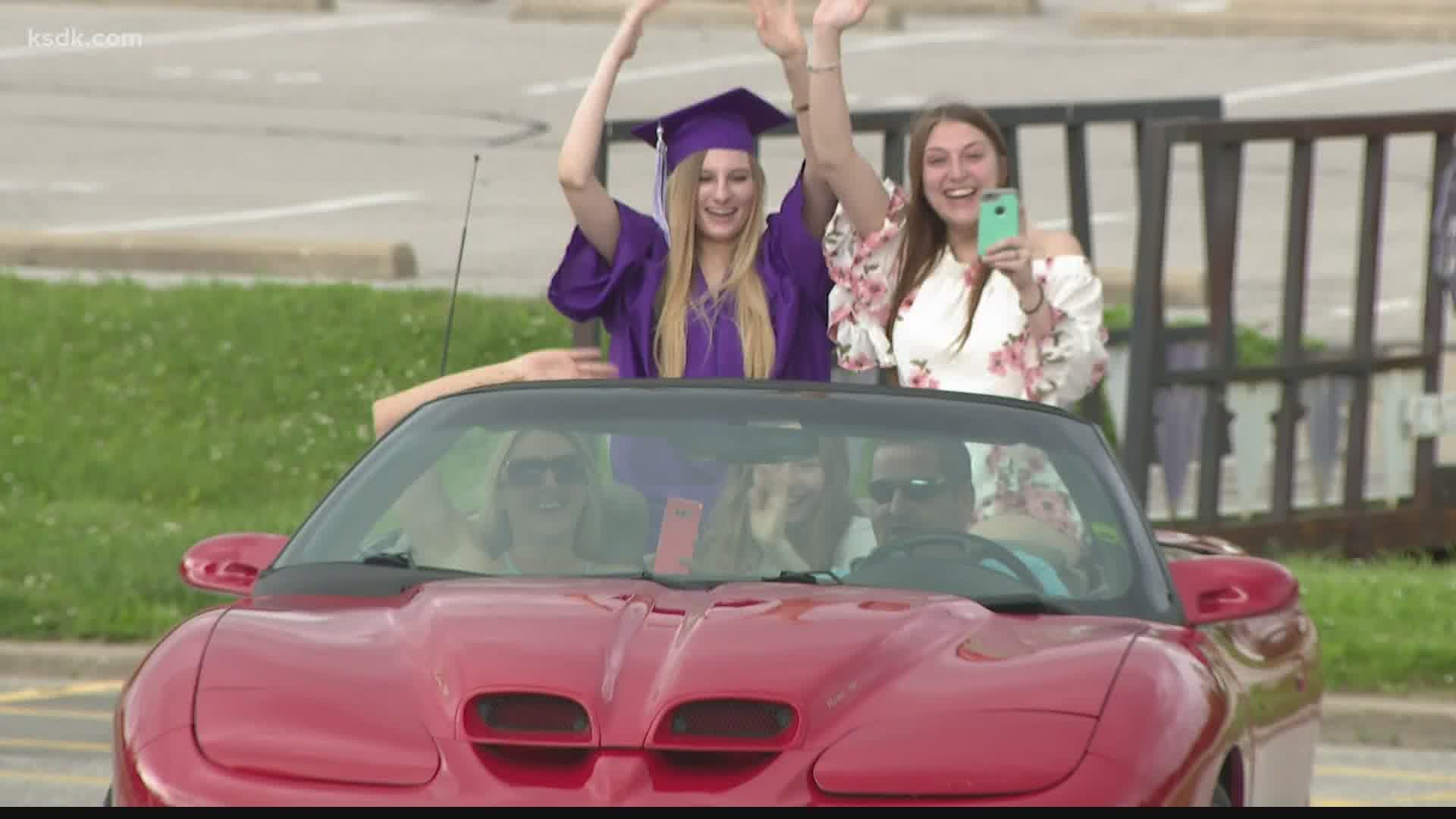 Graduates are driving by in caps and gowns to get their diplomas and have a picture taken.