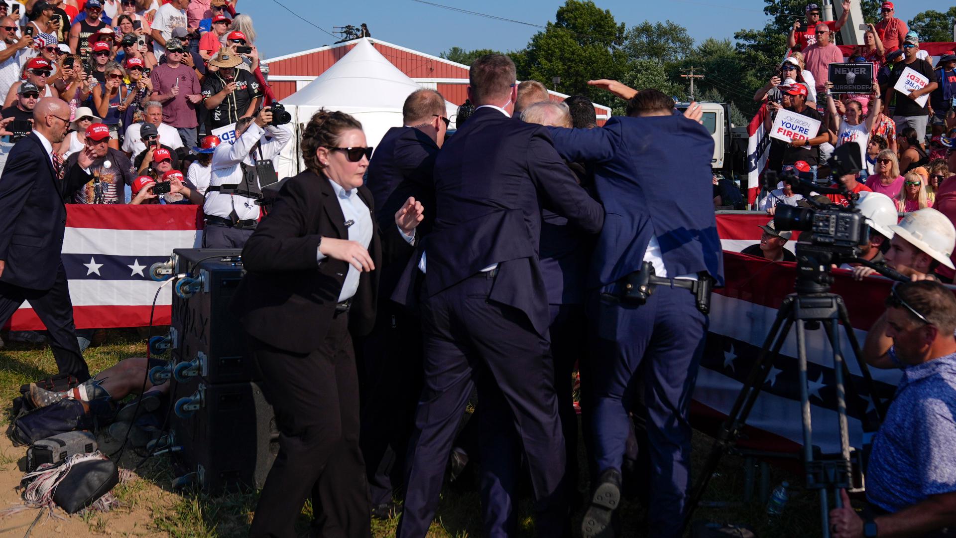 Video shows people ducking down and cheering when Trump stands up. Law enforcement officers go into bleachers.